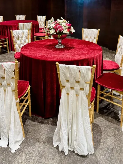 A beautiful dining setup with tables covered in rich red velvet and chairs elegantly draped in white fabric, creating a royal and romantic look.