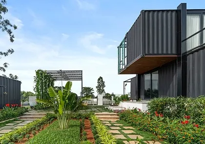 A wide shot showing the different modules of the container home and their arrangement on the property. The lush landscaping and clear blue sky emphasize the project's focus on indoor-outdoor living.