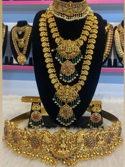 A three-piece bridal set with two layered necklaces and a wide vaddanam. The green beads add a touch of color to the antique gold finish.