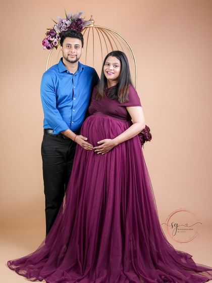 A classic full-length portrait of the expecting couple. The rich purple gown and the partner's simple attire create a balanced and elegant look.