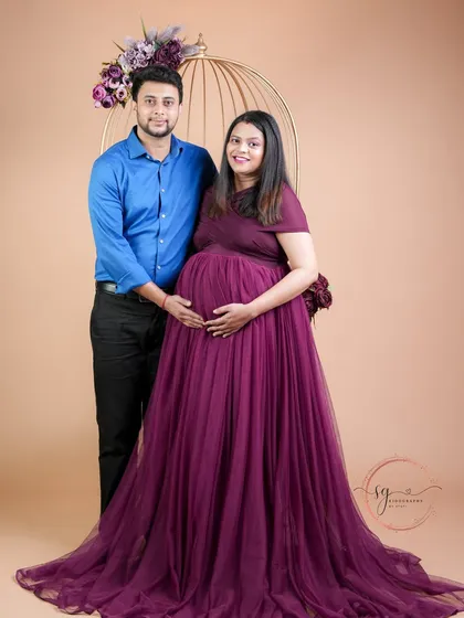 A full-length portrait showcasing a beautiful maternity gown. This shot gives a wonderful view of the elegant dress and the proud stance of the parents-to-be in a studio setting.