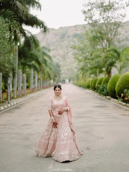 A stunning full-length portrait of the bride in her pink lehenga on a road lined with palm trees, a perfect destination wedding shot.