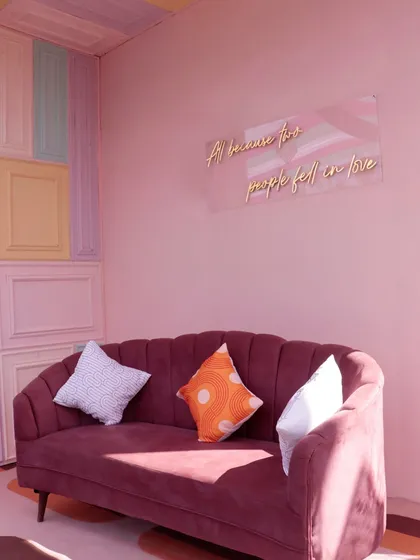 A cozy photo corner with a plush sofa, a wall of pastel-colored panels, and a romantic neon sign, offering a sweet spot for pictures.