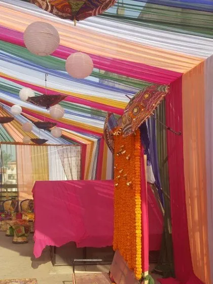 We can cover large open areas or terraces with colorful fabric tenting for Ladies Sangeet, Haldi, or Mehndi functions. This setup uses multi-colored drapes with hanging umbrellas and lanterns to create a festive canopy.