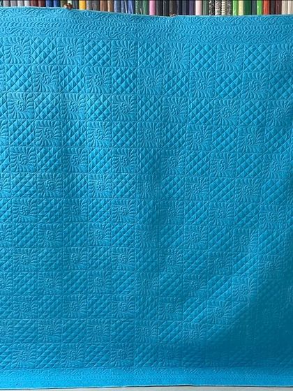 The solid teal back of the quilt, which beautifully showcases the intricate quilting designs.