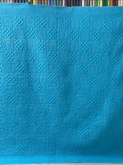 The solid teal back of the quilt, which beautifully showcases the intricate quilting designs.