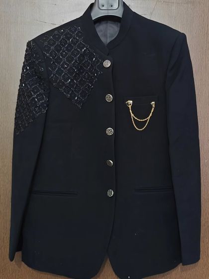 A closer look at this black Jodhpuri-style suit jacket. It features a mandarin collar, intricate shoulder beading, and a pocket chain for a touch of regal flair.