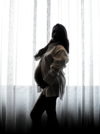 A stunning silhouette of an expecting mother against the soft light of our studio's sheer curtains. This artistic approach to maternity photography creates powerful and elegant images.