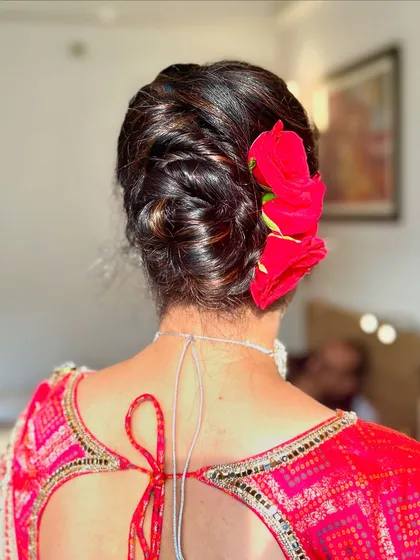A beautiful party hairdo featuring an intricate low bun adorned with a fresh red flower. This classic style is perfect for pairing with a traditional saree.