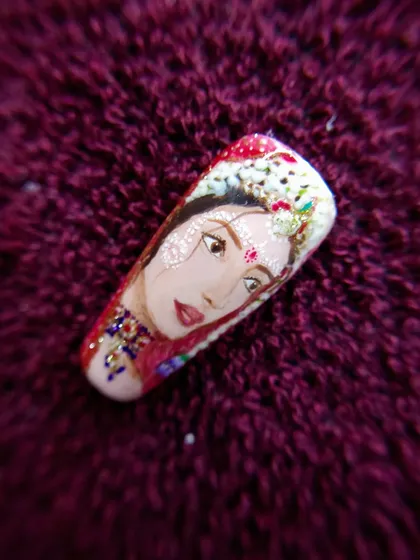 A close-up of a hand-painted bridal portrait, capturing the delicate features and jewelry of a traditional Indian bride on a single nail.