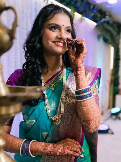 A close-up of a Maharashtrian bride adjusting her nose ring, her smile radiating happiness and excitement.