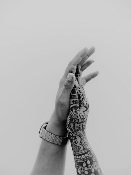 A beautiful black and white close-up of hands. This shot highlights the intricate henna and the gentle connection between the couple, telling a story without showing their faces.
