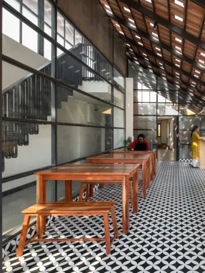 This is the cafeteria area within the Earthen Spirit co-living space, located on the open terrace. We used simple wooden furniture and patterned cement tiles to create a welcoming community area. The glass wall provides a clear view of the new double-height staircase, making the entire space feel connected and expansive.
