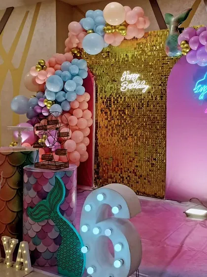 A side view of a mermaid-themed sixth birthday, showing the shimmering gold backdrop and pastel balloon arch.