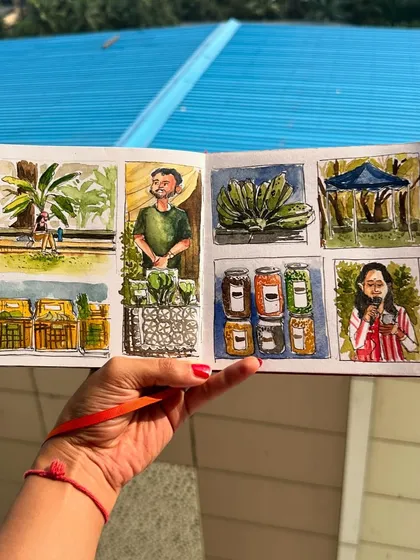 Holding up my farmer's market sketchbook spread against a bright blue roof, making the watercolour colours pop.