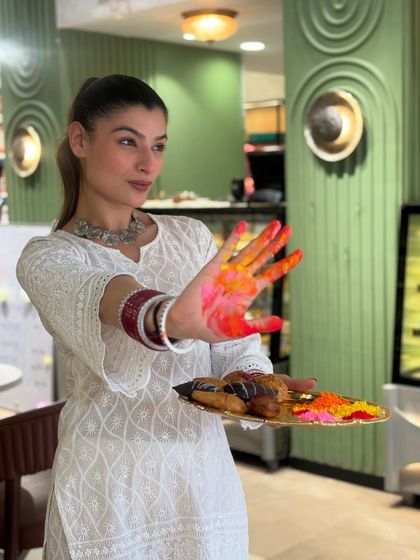 This Holi, don't bring boring gujiyas. A model playfully presents a platter of our assorted, colorful, and delicious Holi sweets.