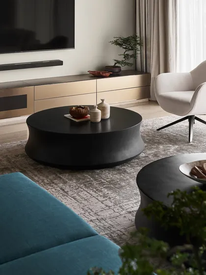 A close-up of one of the "Orbit" coffee tables, crafted from black concrete. Its soft, curved form provides an organic counterpoint to the linear furniture, adding sculptural interest and a tactile quality to the living space.