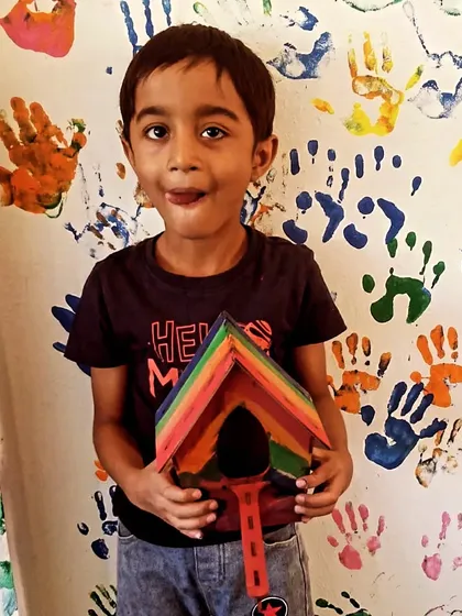 A young builder proudly shows off the colorful birdhouse he constructed and painted. We encourage every child to express their unique style, and this vibrant rainbow design is a perfect example of that creative freedom.