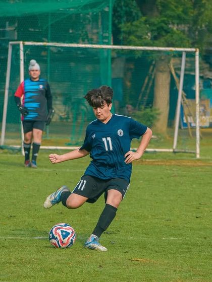 An older player practices a penalty kick, focusing on technique and power under the guidance of a coach.