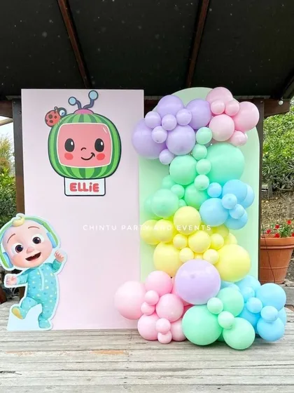A Cocomelon themed birthday party with pastel rainbow balloons. This outdoor setup features character cutouts of JJ and the iconic watermelon TV.