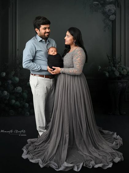 A full-length portrait of a new family. The mother's flowing grey gown and the classic dark backdrop create a sophisticated and elegant look for their first family photo.