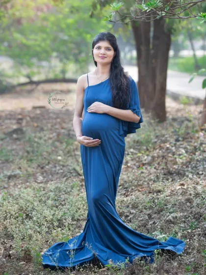 A graceful portrait in a beautiful blue gown. The one-shoulder design and long train add a touch of elegance to this outdoor maternity photo in the woods.
