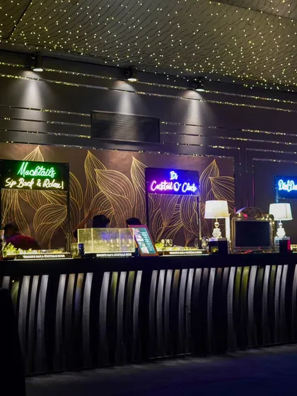The bar is always a statement piece. This setup features a sleek black bar, custom neon signs, and a backdrop of gold-leaf patterns, all under a canopy of fairy lights.