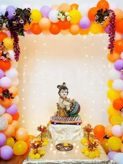A Janmashtami decoration featuring a balloon arch in vibrant colors around a Krishna idol, with fairy lights adding a magical glow.