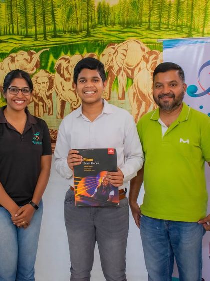 A student holding his ABRSM piano exam book stands with his teachers.