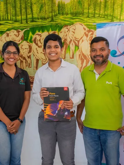 A student holding his ABRSM piano exam book stands with his teachers.