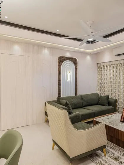 This living room in Seawoods features a subtle and calming color palette with an olive green sofa and arched wall niches. The design uses soft curves and clean lines to create a serene and modern living space.