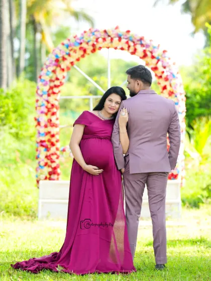A classic couple's portrait in front of a floral arch. The mother-to-be is wearing a wine-colored gown, and the pose is full of love and connection.
