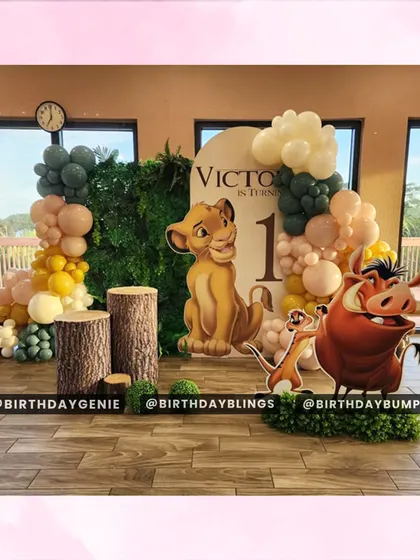 This Lion King first birthday theme uses natural elements like tree stump plinths and a leafy green wall. The setup is framed by a large window, blending the indoor decor with the outdoor scenery for a beautiful effect.