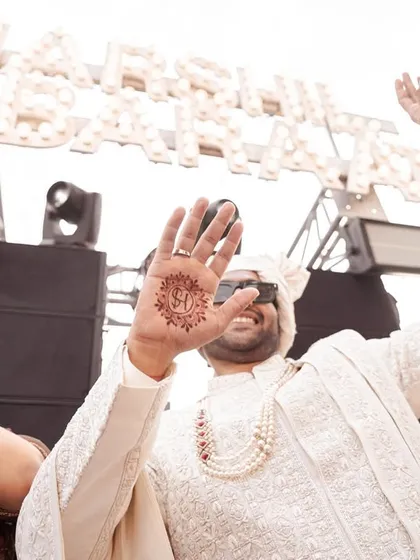 The groom shows off his mehendi, with the bride's initial creatively designed on his palm. This fun, candid shot captures a modern tradition and the festive spirit of the wedding.