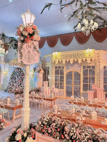 A wide shot of the Parisian-themed party, with custom patisserie facades, elegant street lamps, and tables set for a magical tea party.