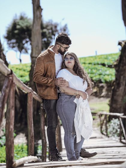 A stylish couple poses on a rustic wooden bridge in the Ooty hills, blending fashion with nature.