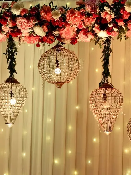 A beautiful backdrop detail, with hanging crystal lanterns and a lush border of pink and red flowers against a fairy light curtain.