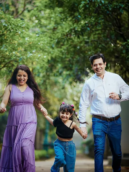 An action shot of a family holding hands and running joyfully towards the camera along a park path.