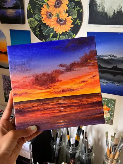 A vibrant sunset painting capturing the deep blues of the sky meeting the fiery oranges and purples of the horizon over the ocean. This acrylic on canvas piece is all about the dramatic and beautiful colors of a beach sunset.