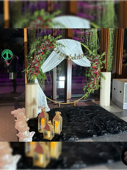 A sophisticated floral ring backdrop for a client's send-off party. This design uses a circular gold frame adorned with fresh red roses, baby's breath, and lush greenery, paired with elegant white draping. It creates a perfect, stylish photo opportunity for any celebration.