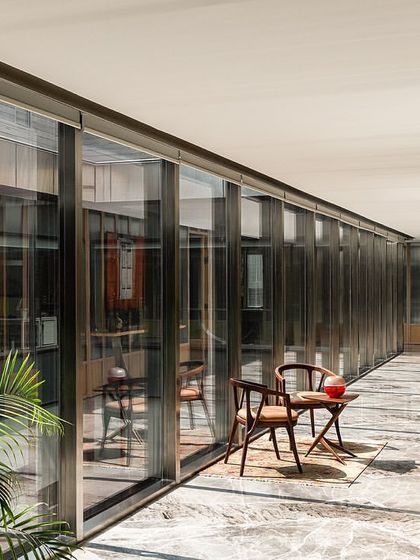 The corridor on the director's floor of the Stainless Steel Office features striking greyish-white marble and a fluted glass and wood paneled wall. This combination of materials creates a sophisticated and distinct aesthetic for the executive level.