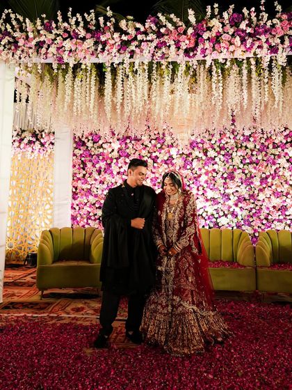 A happy, smiling portrait of the couple in front of their stunning floral reception stage. Their joy is palpable.