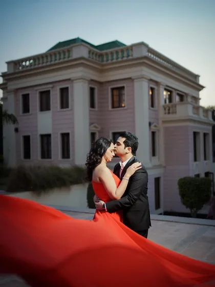 A classic pre-wedding portrait with a grand architectural backdrop. The flowing red gown adds a pop of color and drama to this romantic embrace.