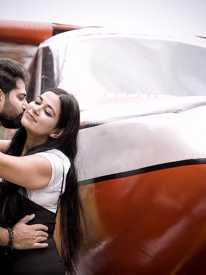 A romantic kiss on the cheek, with a couple embracing in front of a small airplane prop.