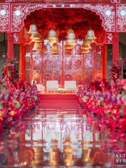 The aisle view of the 'Kaanch Bagh' mandap, with its mirrored walkway reflecting the dramatic red florals and hanging temple bells. This created a powerful and sacred path for the couple.