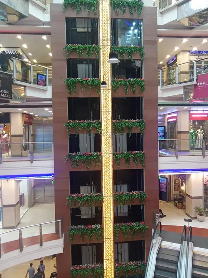A multi-story shopping mall elevator shaft decorated with our artificial hanging flower boxes. This large-scale installation adds color and life to the mall's central atrium.