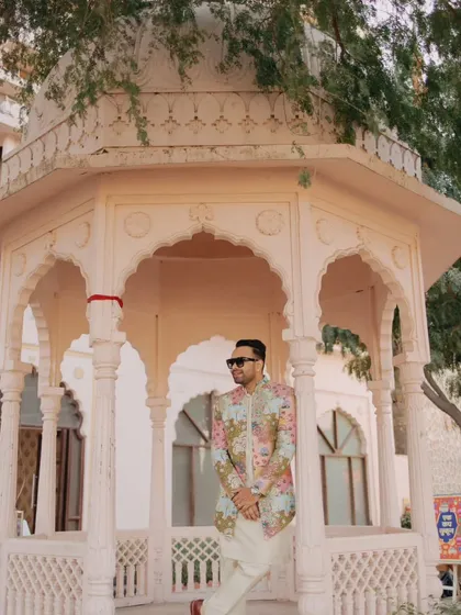 A stylish portrait of the groom in his colorful printed jacket, posing with confidence in a palace courtyard.