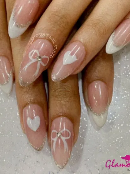 An elegant and romantic French manicure with a sheer pink base, sparkling silver tips, and accent nails featuring hand-painted white hearts and bows.