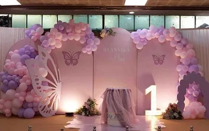 This large-scale butterfly theme stage decoration is perfect for a magical first birthday. It features two large backdrops with soft pastel balloon arches, a giant butterfly wing prop for photos, and a light-up number '1'.