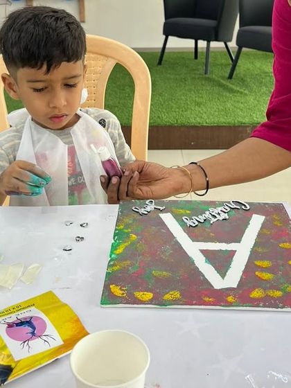 A young boy fully engaged in decorating his initial canvas. We provide stencils and various craft materials to help kids add texture and detail to their paintings.